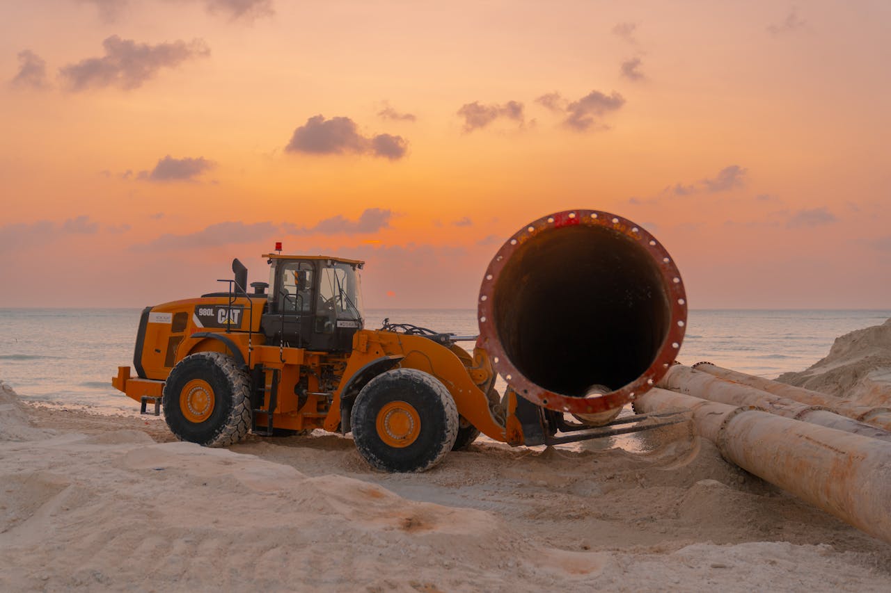 Bulldozer on a beach construction site during a vibrant sunset by the ocean.