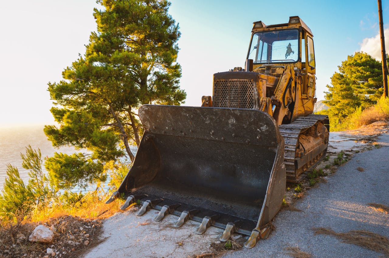 Sturdy bulldozer resting on a scenic roadside by the sea, bathed in warm summer sunlight.